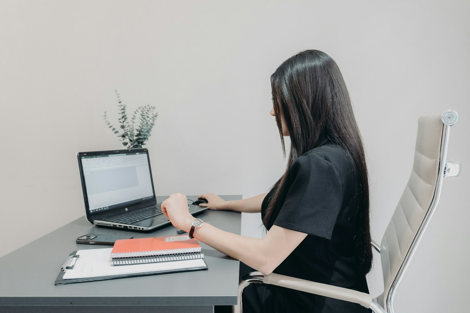 Una donna lavora a un foglio di calcolo su un computer portatile in un ufficio, con quaderni e una cartellina sulla scrivania