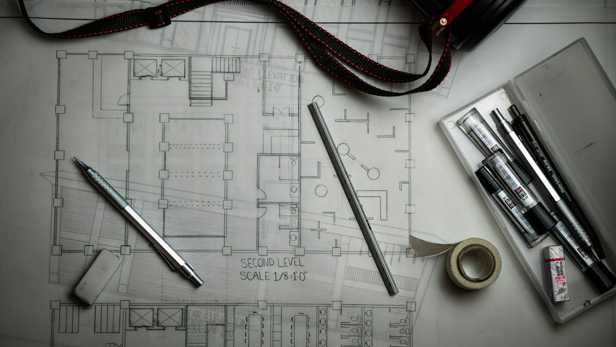 Disegni tecnici architettonici con matite, righello metallico e tubo porta progetti, immagine simbolica del CAD gratuito