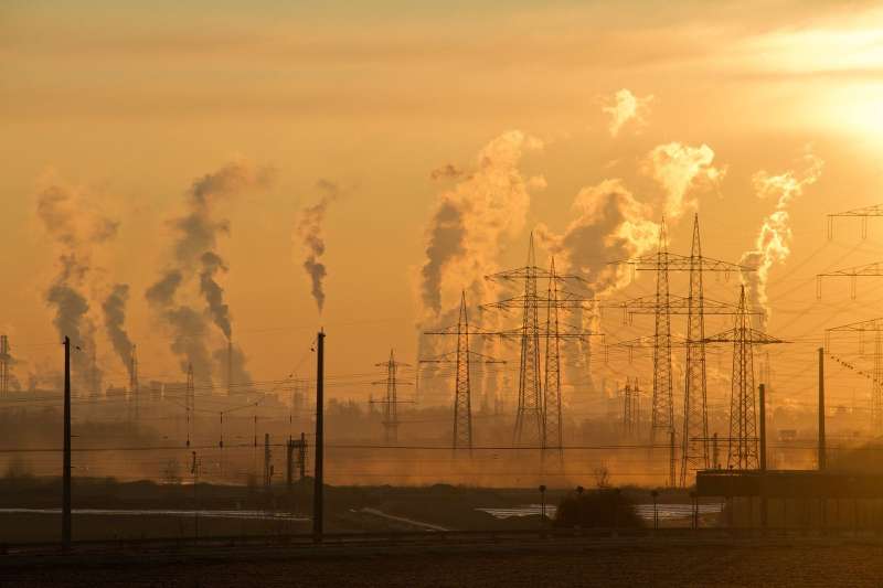 Linee elettriche e fumo industriale controluce al tramonto, simbolo di elettrificazione dei processi industriali