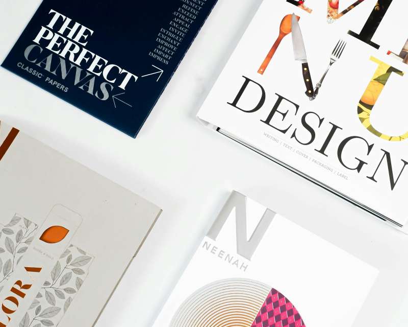 Libri di design e campioni di brochure stampate su un tavolo bianco, immagine simbolica dei materiali impaginati con Microsoft Publisher
