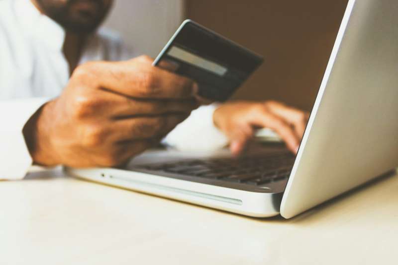 Mani che tengono una carta di pagamento davanti a un portatile durante un acquisto online
