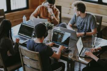 Gruppo di colleghi al lavoro su computer portatili attorno a un tavolo, immagine simbolica di una suite collaborativa per l'ufficio